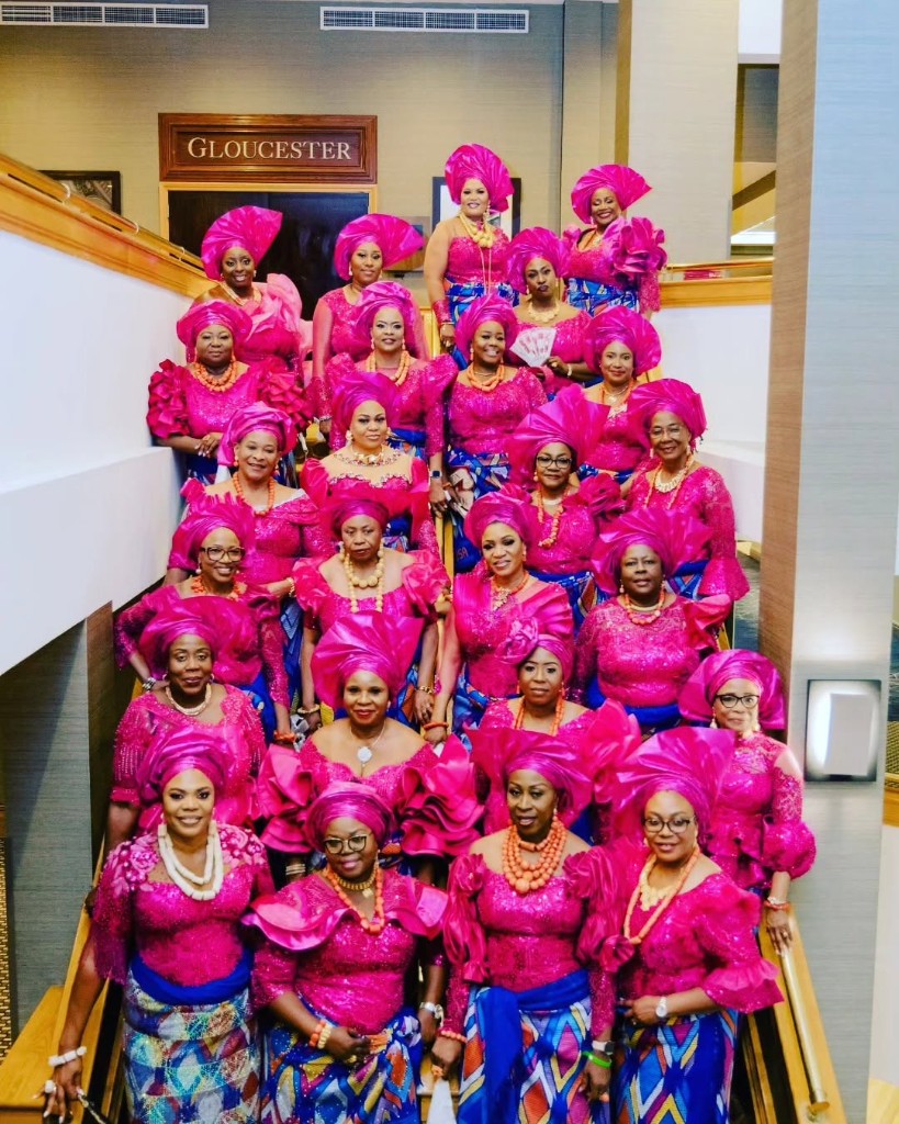 Women in magenta gele and lace blouses posed on a staircase